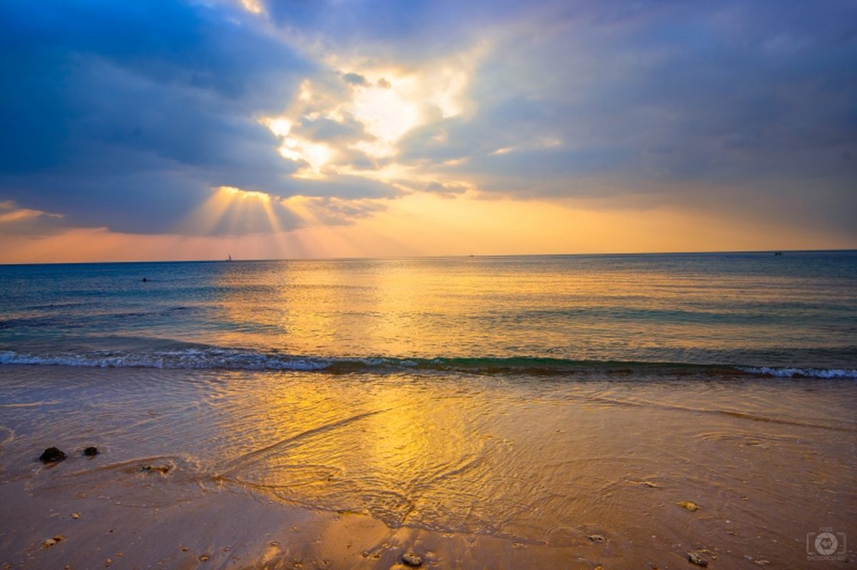 Golden sunlight breaking through clouds over a calm beach